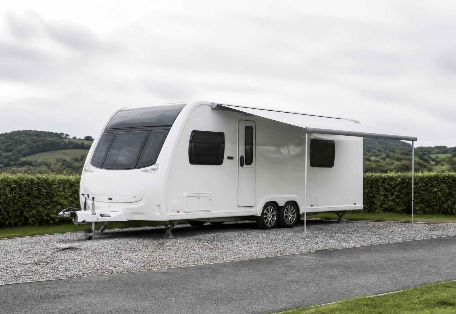A white twin-axle touring caravan with its awning out on a hardstanding pitch